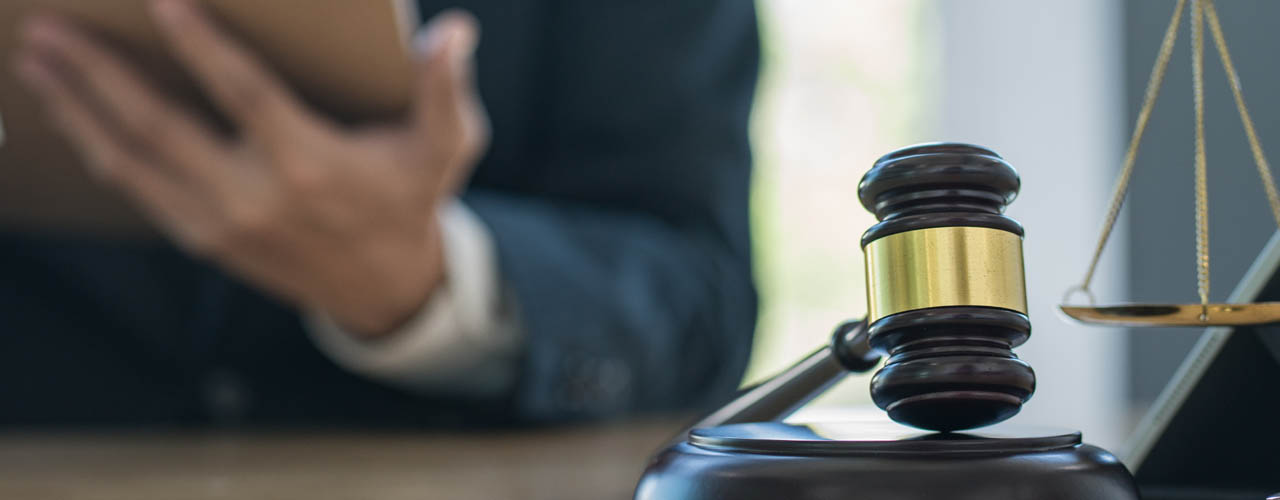 A gavel and a set of scales sitting on a desk in front of a man in a suit.