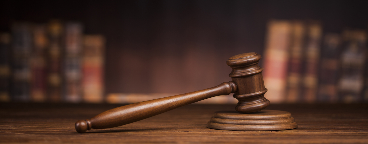 A gavel sitting on a sounding block in front of a shelf of books.